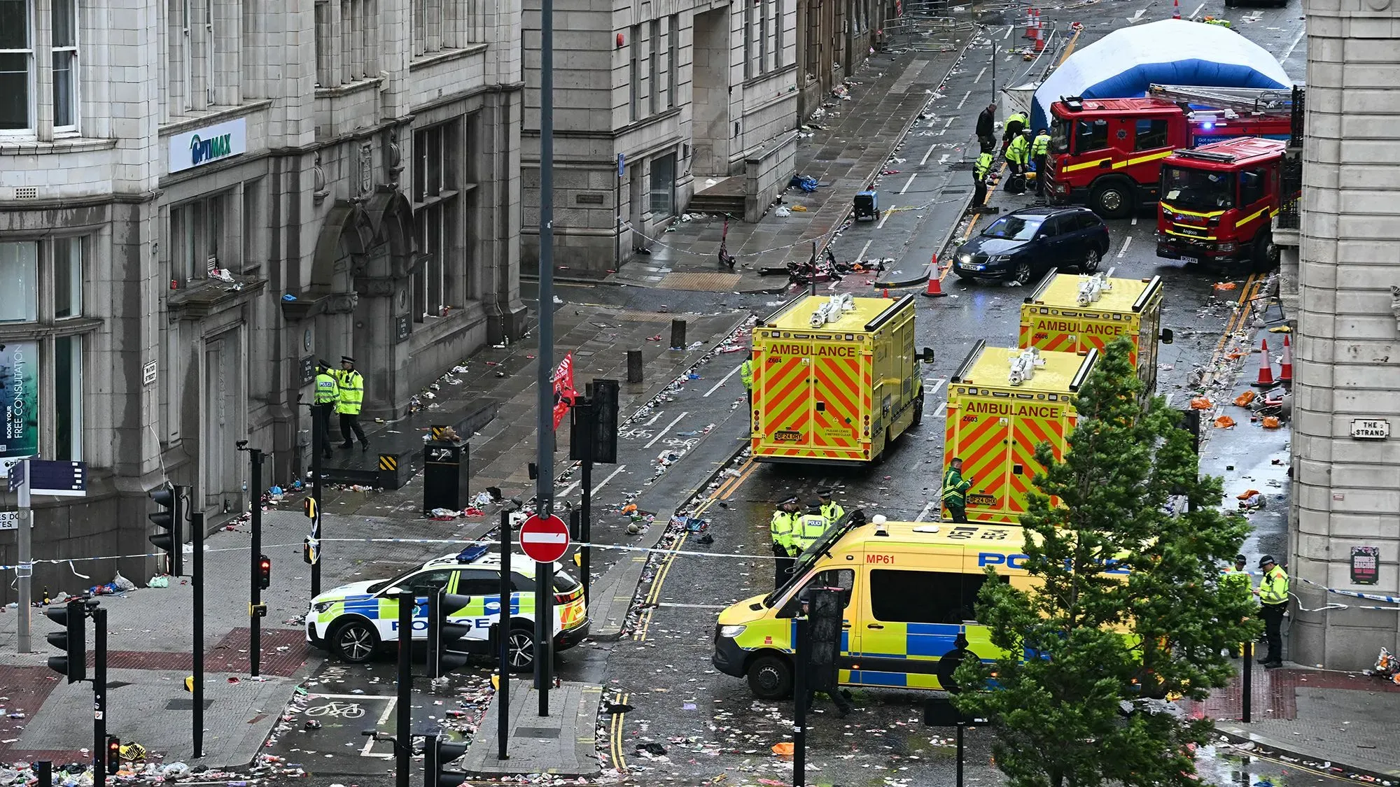 مشهد لشارع في ليفربول بعد حادث الدهس، يظهر سيارات إسعاف ورجال شرطة في موقع الحادث، مع وجود فوضى في الشارع.