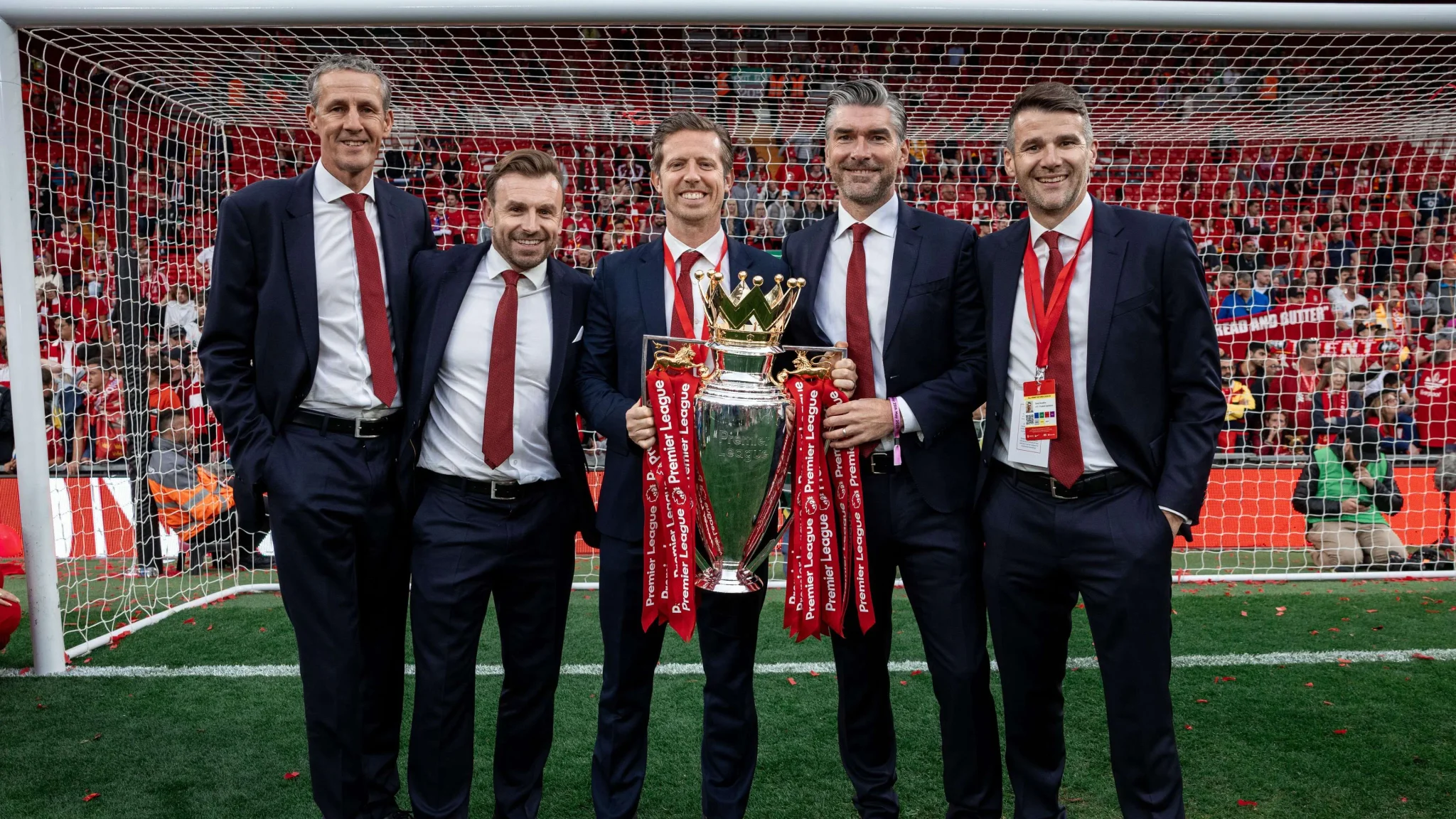 مجموعة من المسؤولين الإداريين في ليفربول يحتفلون بحمل كأس الدوري الإنجليزي الممتاز على ملعب أنفيلد، في لحظة نجاح رياضية قبل انتقال ريتشارد هيوز إلى الهلال السعودي.