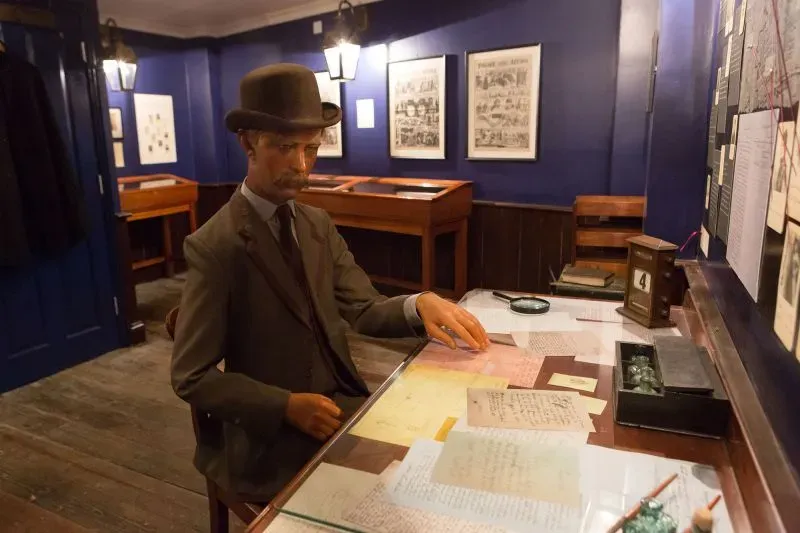 تمثال شمعي لرجل يرتدي قبعة، يجلس أمام طاولة مليئة بالرسائل والمستندات، داخل متحف مخصص لجاك السفاح في لندن.