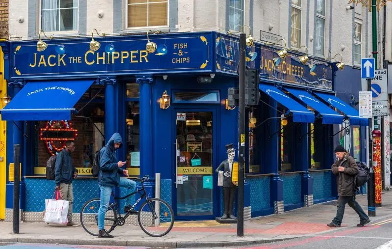مطعم "جاك ذا تشيبر" للسمك والبطاطس في لندن، مع لافتة زرقاء بارزة. يتواجد زبائن أمام المطعم، ويعكس الثقافة السياحية المرتبطة بجرائم جاك السفاح.