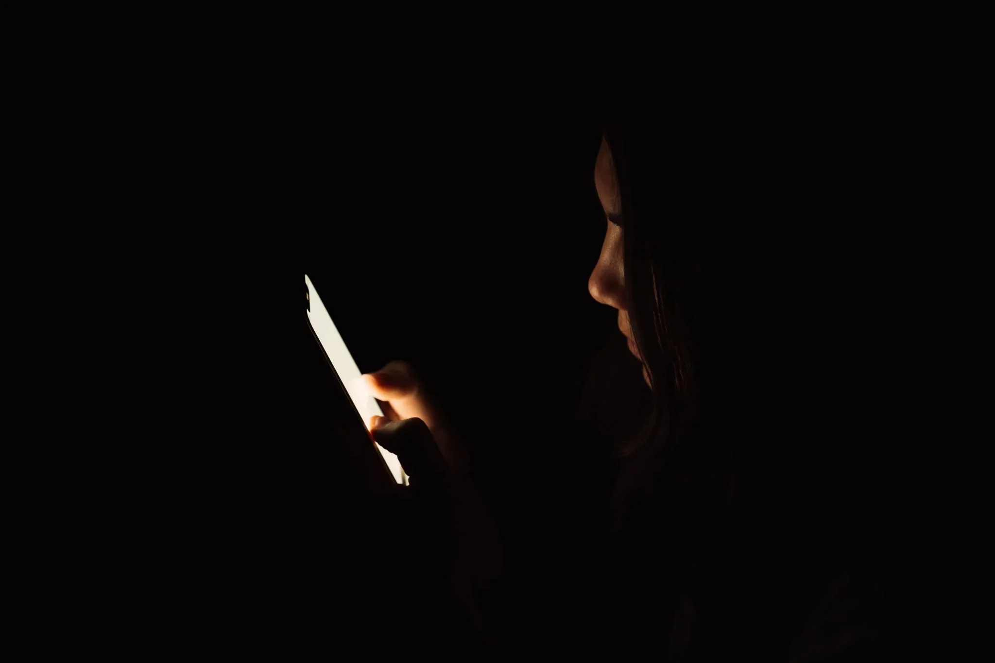 امرأة في الظلام تركز على شاشة هاتفها الذكي، تعكس تجربة الوحدة والتواصل الاجتماعي في العصر الرقمي.