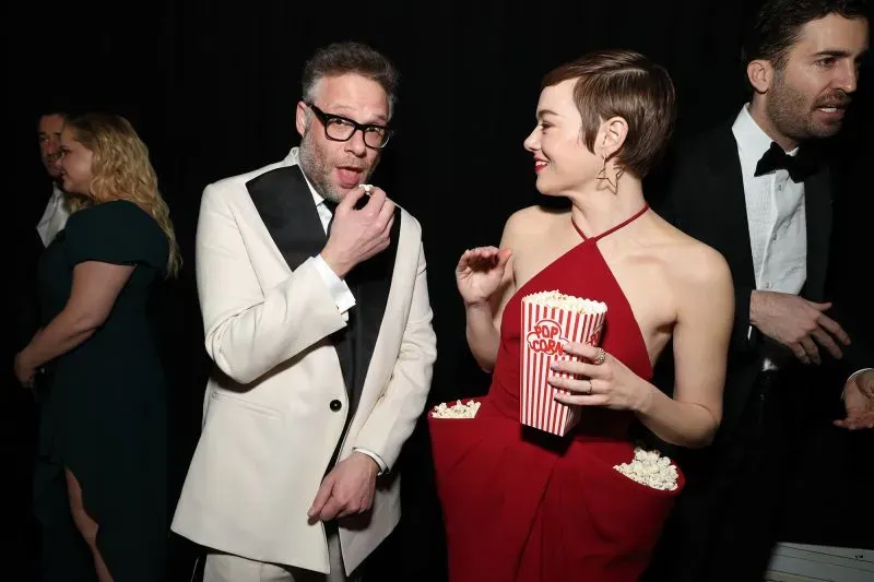 إيما ستون ترتدي فستانًا أحمر بتصميم مبتكر يحتوي على جيوب مملوءة بالفشار، متفاعلة مع الحضور خلال احتفال ذكرى برنامج Saturday Night Live.