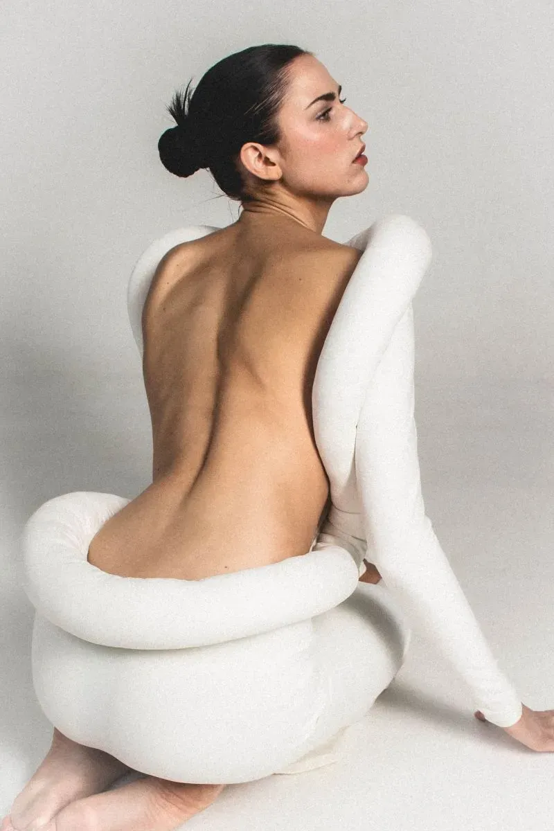 فستان أبيض مبتكر مع تفاصيل هندسية، يظهر امرأة تجلس مع تسريحة شعر بسيطة، يعكس أسلوباً عصريًا ومميزًا في الموضة.