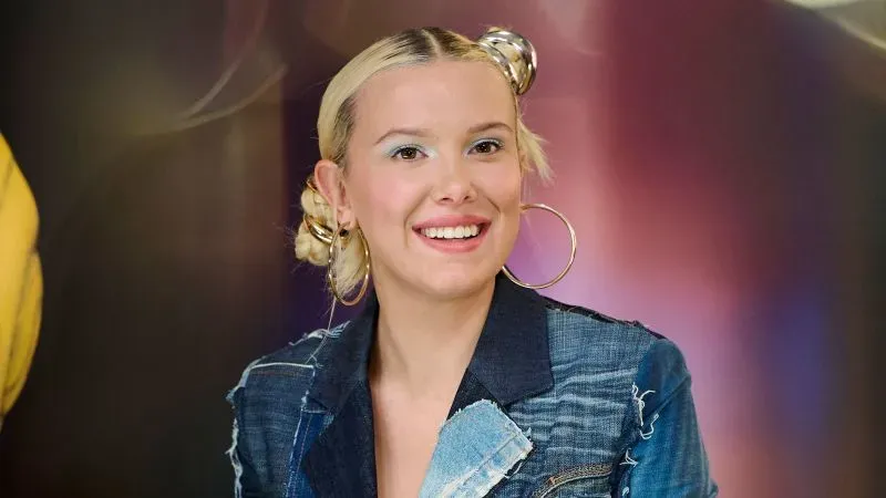 تظهر ميلي بوبي براون بابتسامة، ترتدي ملابس دنيم مع لمسات عصرية، تعكس أسلوب التسعينيات، خلال حدث في مدريد.