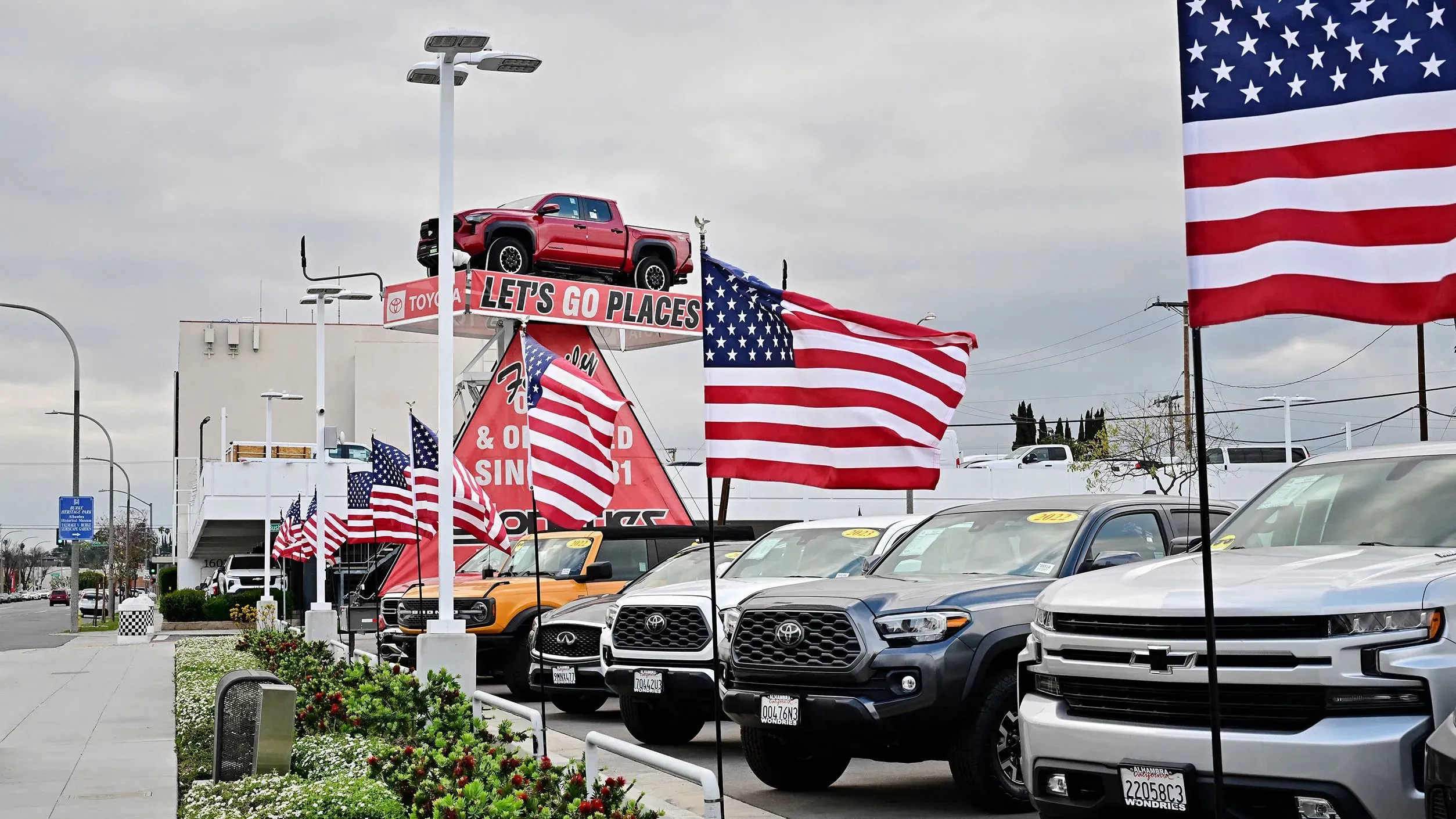 معرض سيارات أمريكي يعرض سيارات جديدة مع لافتة ترويجية، محاط بأعلام أمريكية، في ظل توقعات بزيادة الأسعار بسبب التعريفات الجمركية.