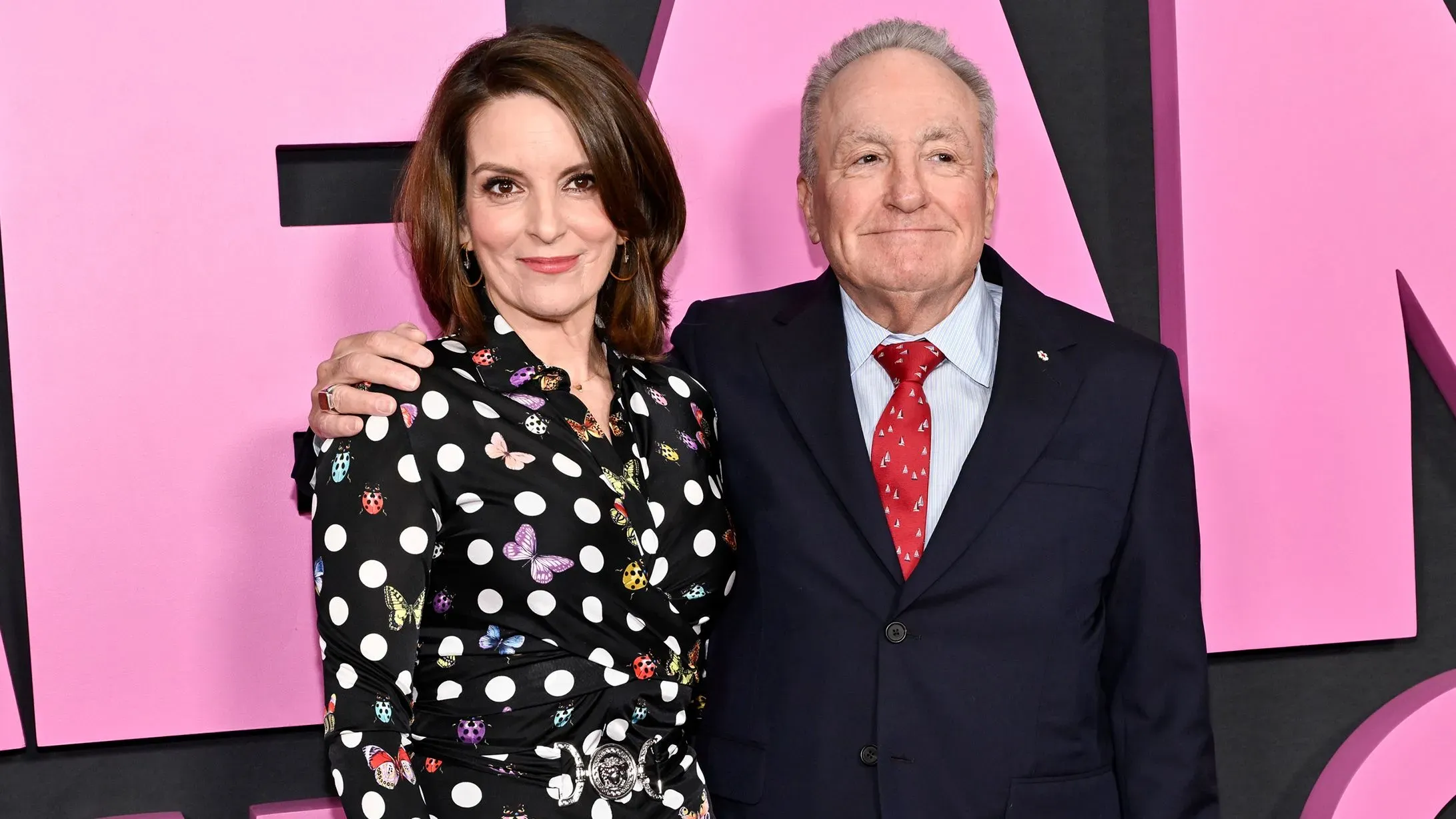 تينا فاي ولورن مايكلز يتبادلان الابتسامات في حدث، مع خلفية وردية، في إشارة إلى شراكتهم الطويلة في برنامج "SNL".