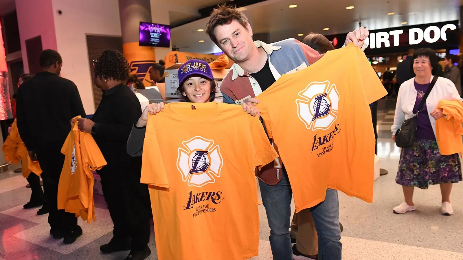 شخصان يحملان قميصين برتقاليين يحملان شعار فريق لوس أنجلوس ليكرز، مع وجود جمهور خلفهم في ملعب كريبتو دوت كوم أرينا.