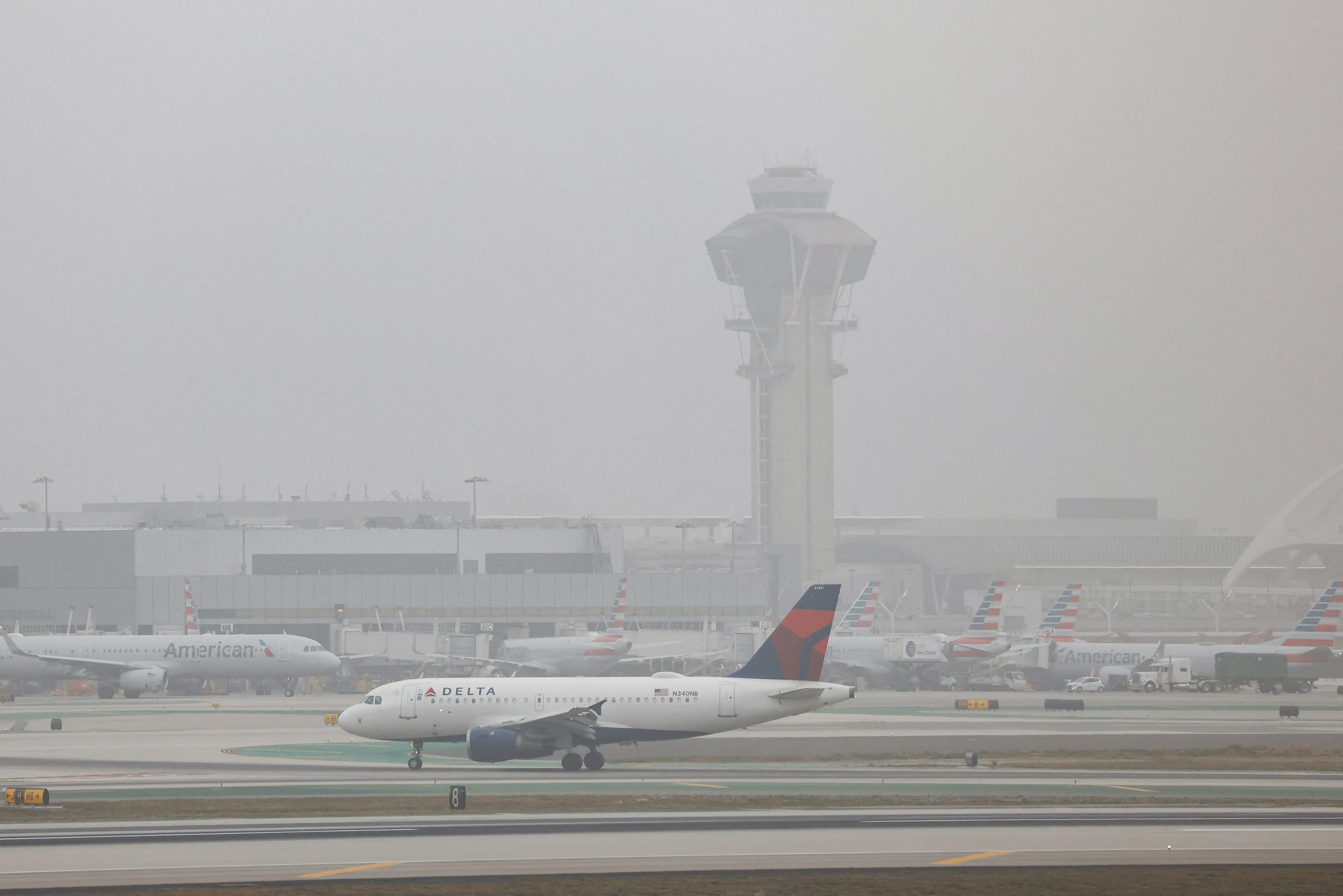 مطار لوس أنجلوس الدولي (LAX) يظهر فيه طائرة تابعة لشركة دلتا، مع أبراج المراقبة والطائرات الأخرى في الخلفية، في سياق تحقيقات تتعلق بتهم تهريب أسلحة.