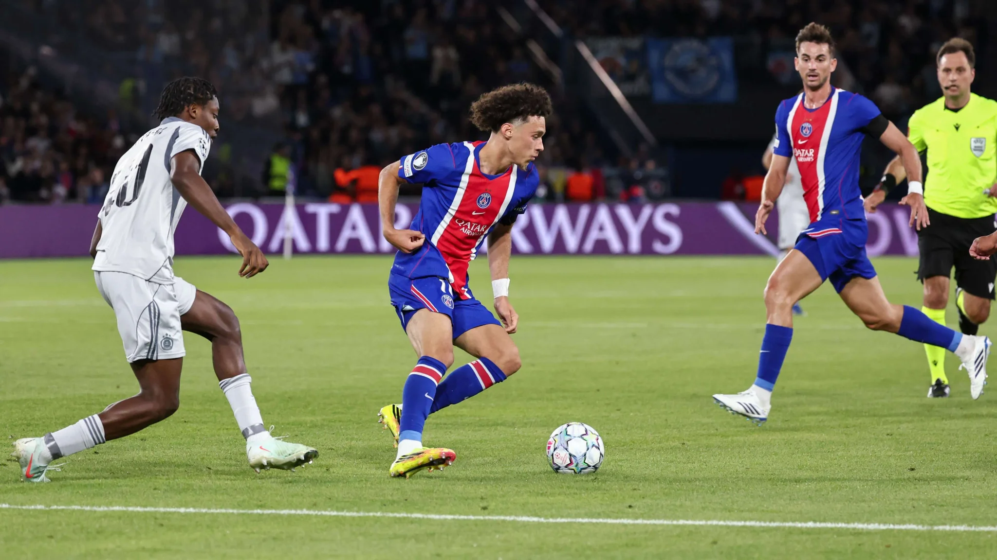 لاعب باريس سان جيرمان Maghnes Akliouche يراوغ الكرة وسط منافسين خلال مباراة دوري أبطال أوروبا، مع تركيز على دوره التكتيكي في الفريق.