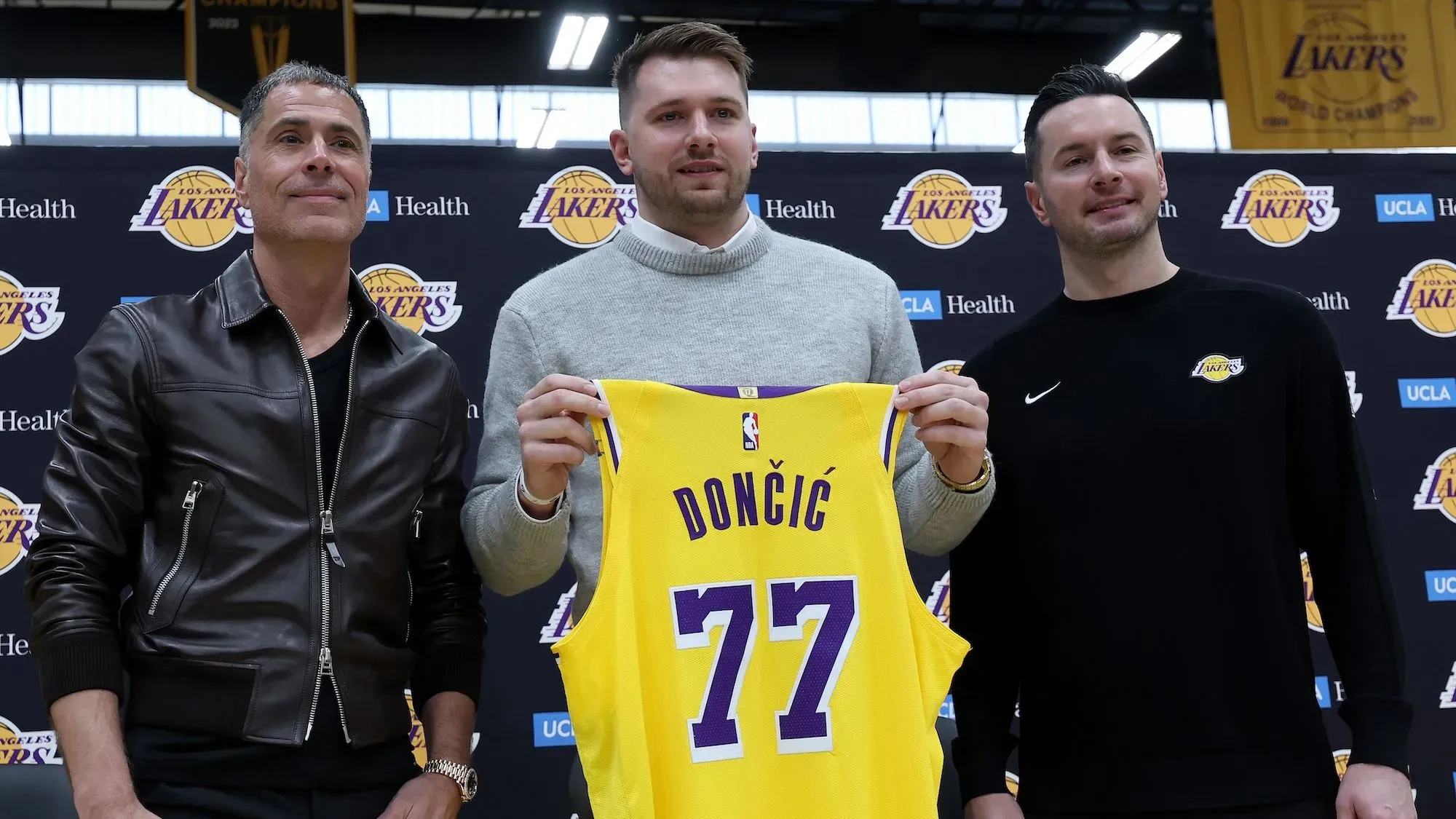 لوكا دونشيتش يحمل قميصه الجديد رقم 77 لفريق لوس أنجلوس ليكرز، مع المدير العام روب بيلينكا ومدرب الفريق، خلال مؤتمر تقديمه.
