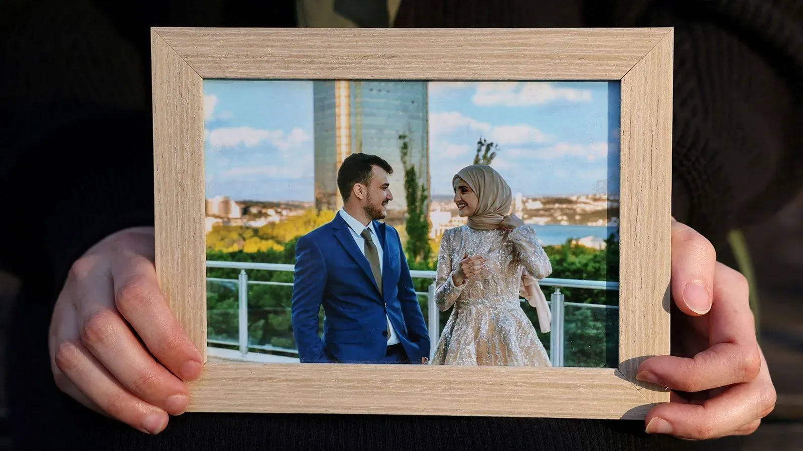 صورة ليد تحمل إطارًا خشبيًا يحتوي على صورة لمحمود خليل وزوجته في حفل زفافهما، تعكس لحظات السعادة التي حُرما منها بسبب احتجازه.