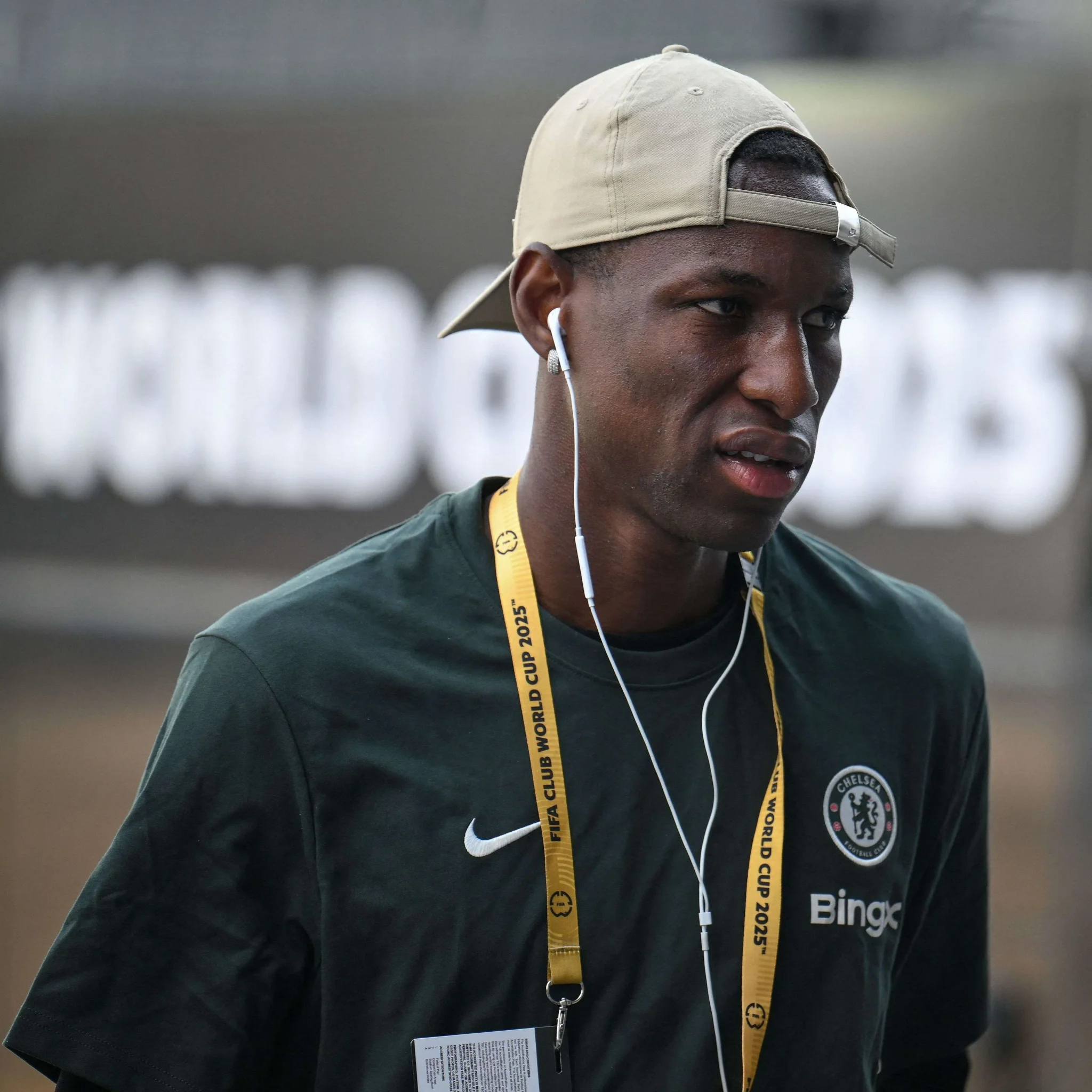 لاعب تشيلسي يرتدي قميص الفريق مع قبعة بيج وسماعات أذن، يحمل بطاقة اعتماد بطولة كأس العالم للأندية 2025.