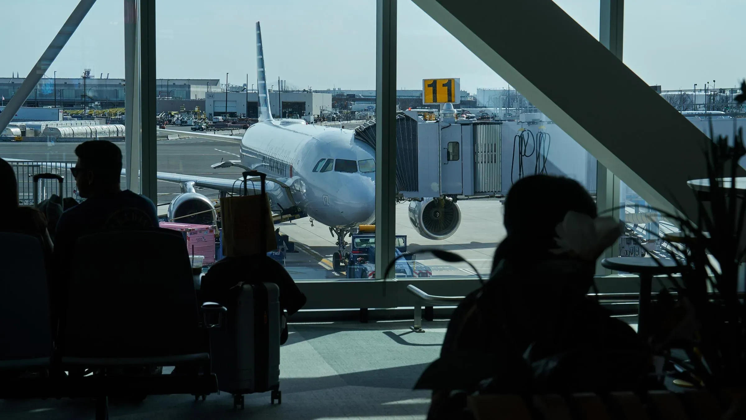 مشهد لمطار نيوارك حيث ينتظر المسافرون في صالة الانتظار، مع طائرة متوقفة عند البوابة رقم 11، وسط تأخيرات في الرحلات.