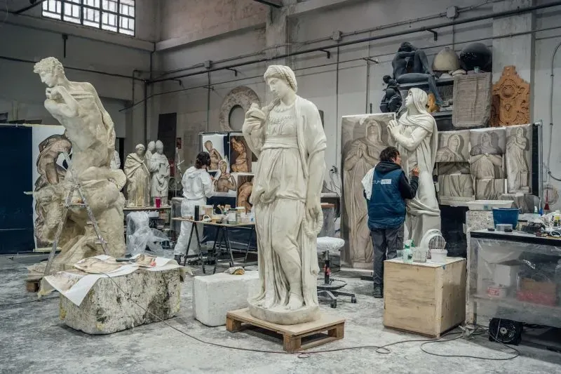 ورشة عمل تضم منحوتات مستنسخة لمايكل أنجلو، مع فنانين يعملون على تفاصيلها، محاطة بأعمال فنية أخرى.