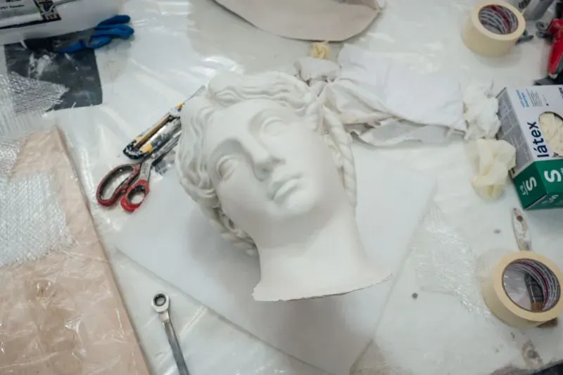 رأس منحوتة من الجبس يمثل أحد أعمال مايكل أنجلو، موضوعة على طاولة مع أدوات فنية، في إطار التحضير لمعرض فني.