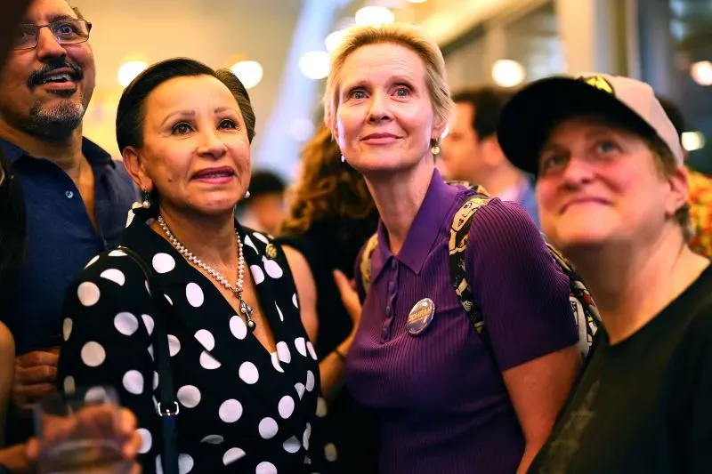 مجموعة من الأشخاص في حفل انتخابي، يبدو عليهم الحماس والترقب، مع خلفية مضاءة وملصقات تدعم زهران ممداني.