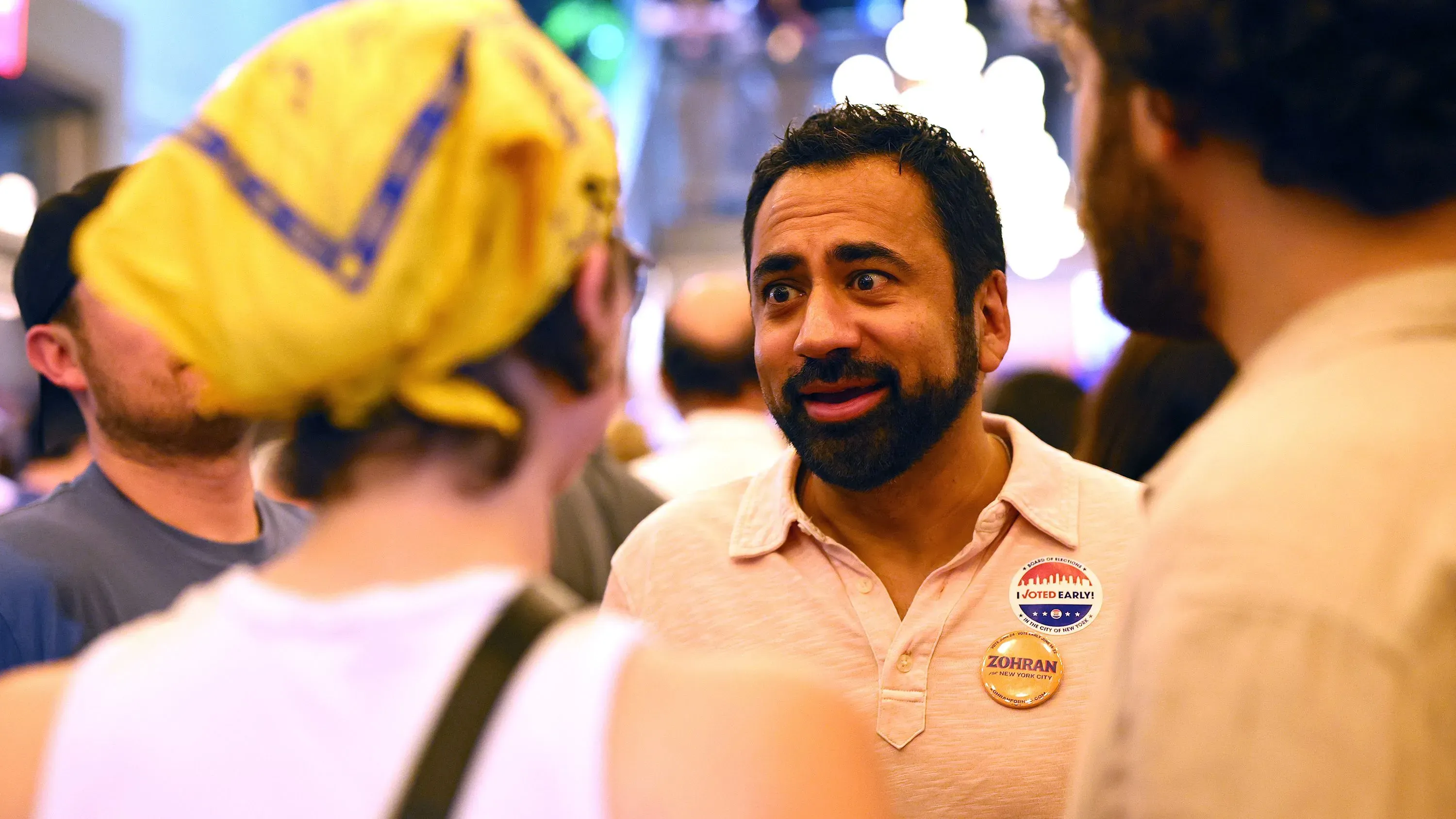 ممداني يتفاعل مع مؤيديه في حفل انتخابي، مرتديًا شارة "صوتت مبكرًا"، وسط أجواء من الحماس والتشجيع.
