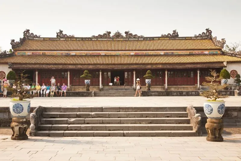 واجهة قصر ثاي هويا في هوي، فيتنام، مع زوار يجلسون على الدرج، يبرز التراث المعماري لأسرة نغوين.