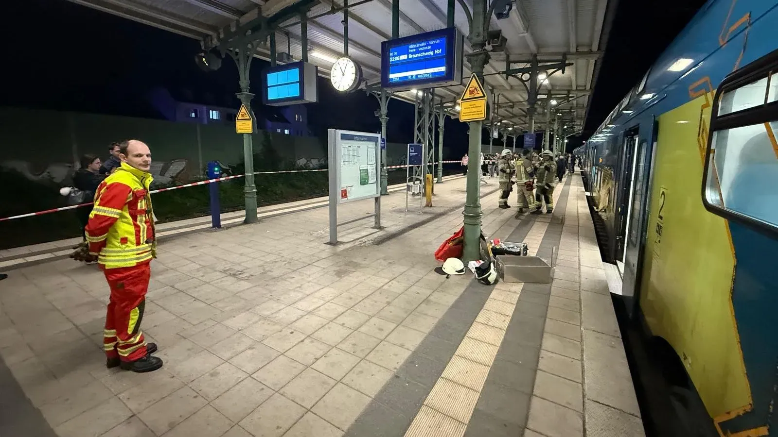رجال الإطفاء في محطة قطار بألمانيا أثناء عملية إنقاذ معقدة لرجل عالق تحت مسند ذراع، مع وجود معدات الطوارئ في الخلفية.