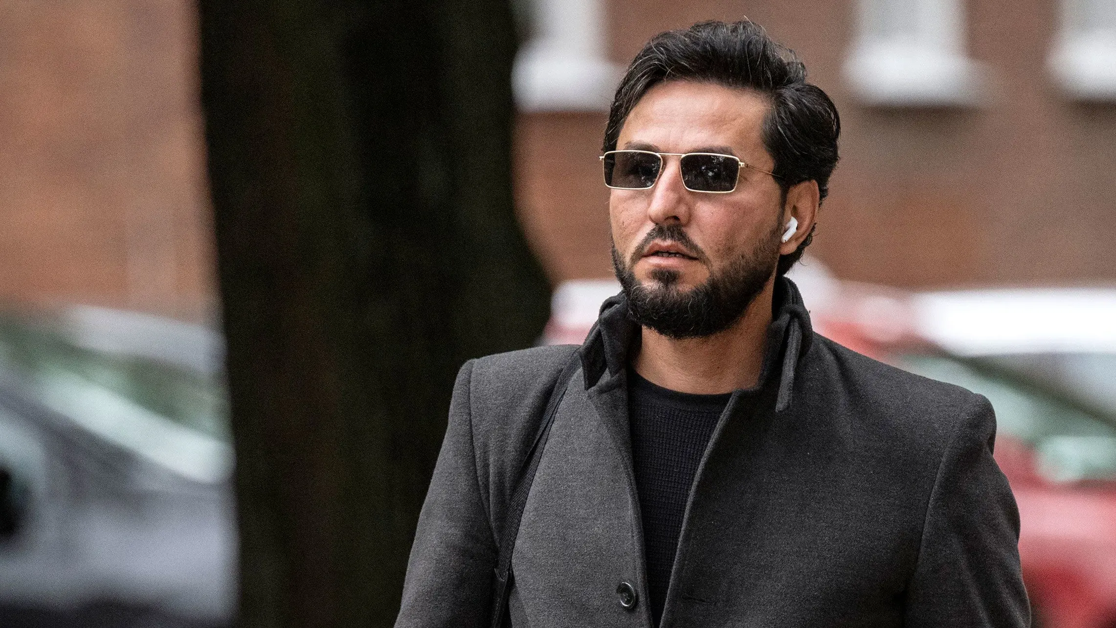 رجل يرتدي نظارات شمسية وسمّاعة أذن، يتجول في منطقة حضرية بعد تقارير عن مقتله في السويد، مما أثار جدلاً حول حرية التعبير.