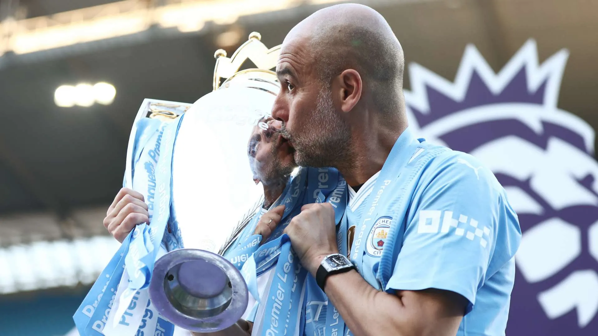 بيب جوارديولا يقبل كأس الدوري الإنجليزي الممتاز مرتدياً زي مانشستر سيتي بعد تحقيق الثلاثية التاريخية موسم 2022-23.