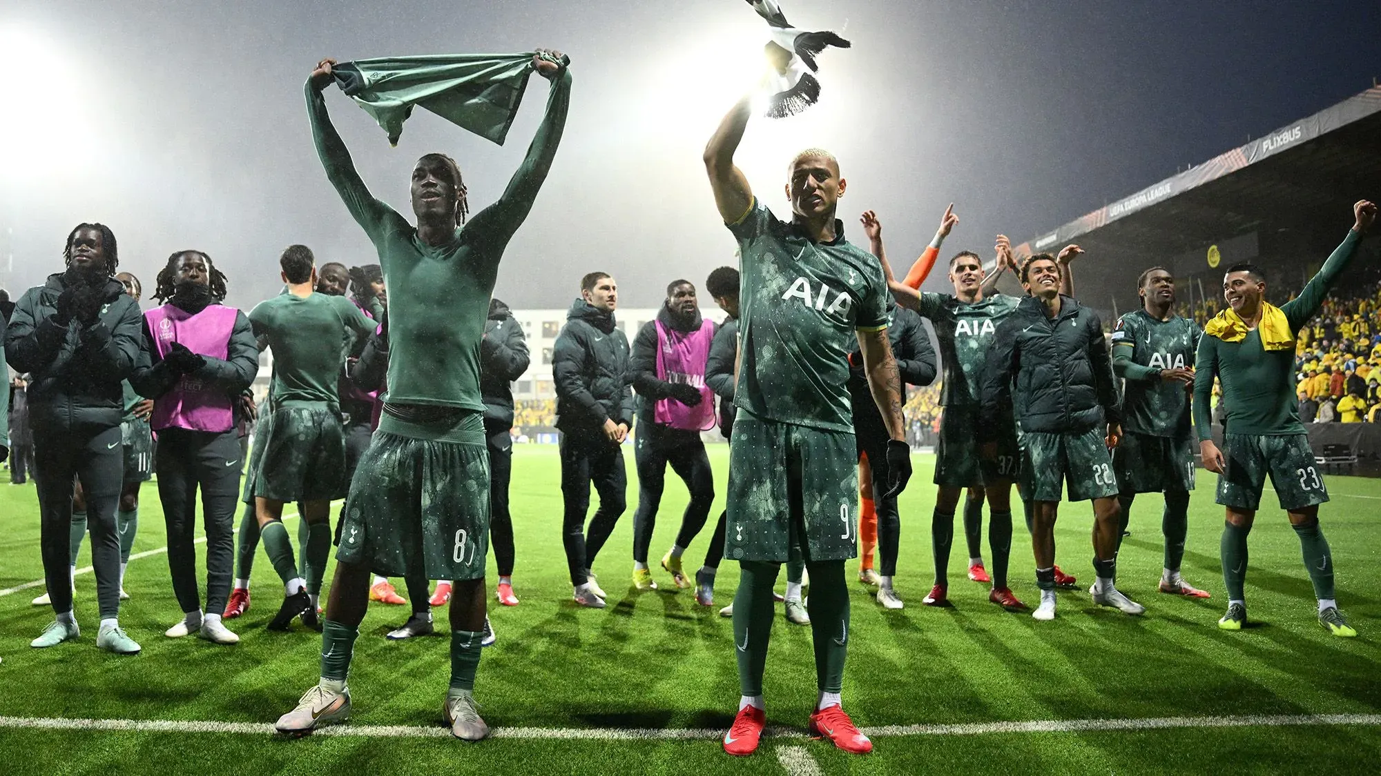 فريق توتنهام يحتفل بعد الفوز في مباراة نصف النهائي، مع اللاعبين يرفعون الأعلام وسط أجواء حماسية في ملعب بارد.