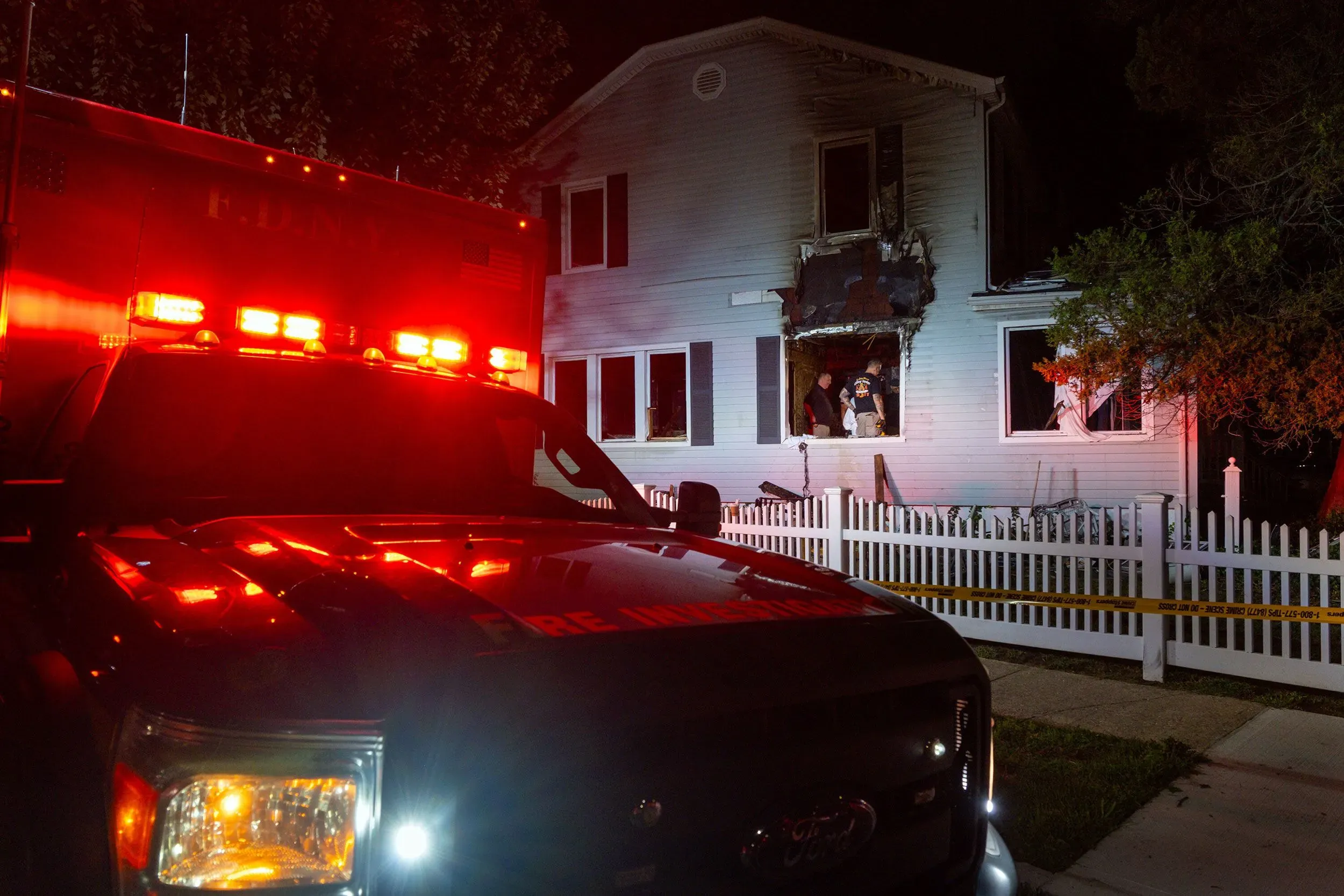 مركبة إطفاء أمام منزل محترق في كوينز، حيث وقع حادث قتل مزدوج لزوجين مسنين، مع وجود رجال الإطفاء في الموقع.