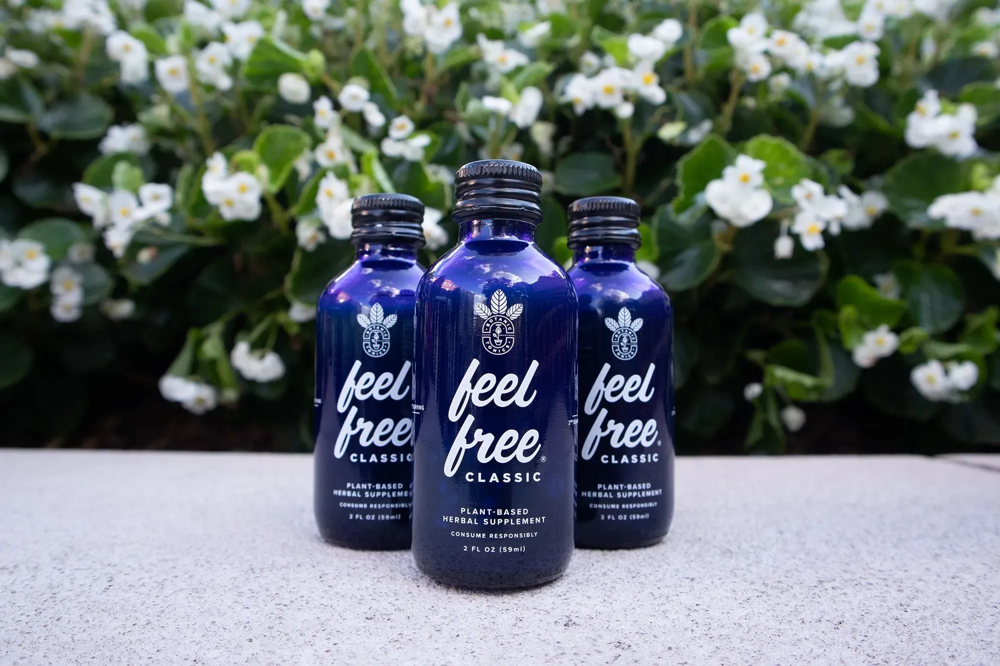 زجاجات من مشروب "Feel Free Classic" العشبي، مع خلفية من الأزهار، تمثل منتجًا يدعي دعم الاسترخاء والتركيز.