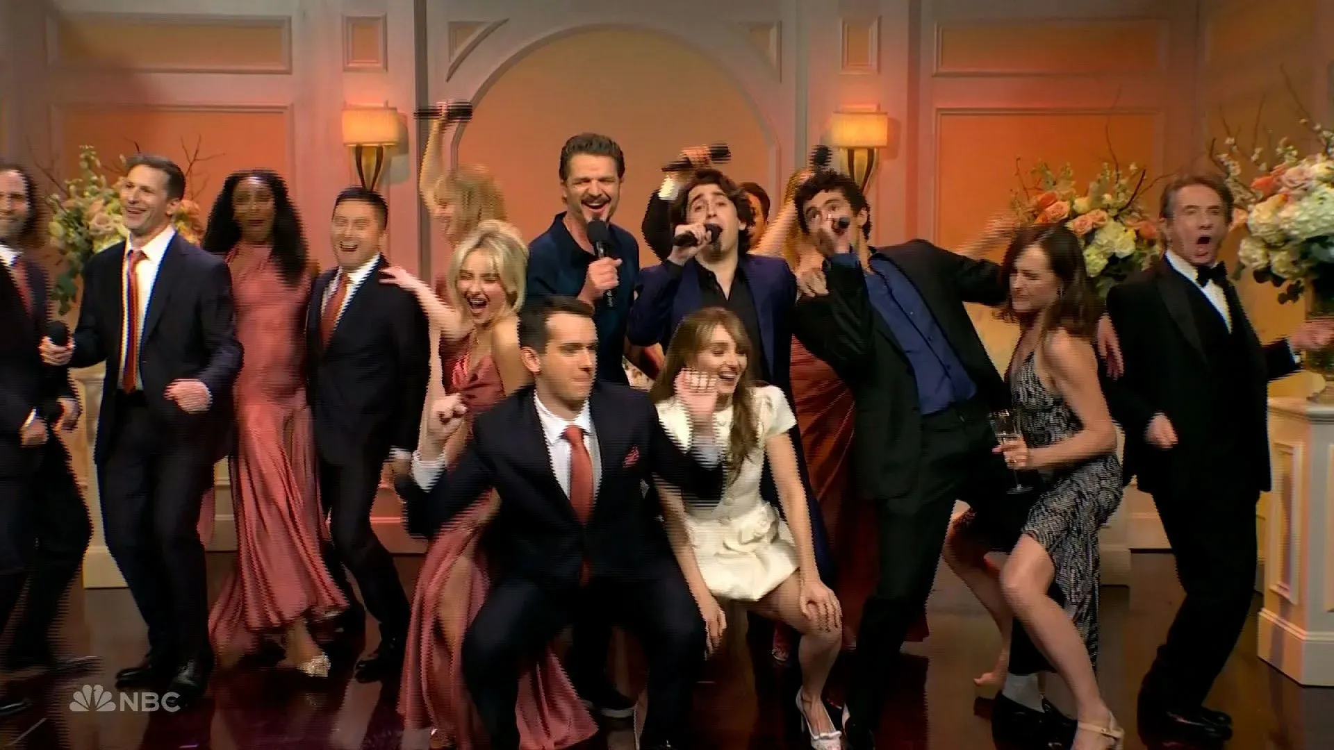 مجموعة من الفنانين يغنون في حفل زفاف، مع التركيز على شخصية دومينغو التي يؤديها مارسيلو هيرنانديز، وسط أجواء احتفالية.