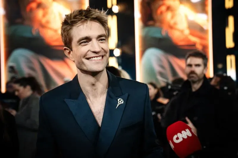 مارك روفالو مبتسم في العرض الأول لفيلم "ميكي 17"، يرتدي بدلة أنيقة، مع خلفية مضاءة تعرض مشاهد من الفيلم.