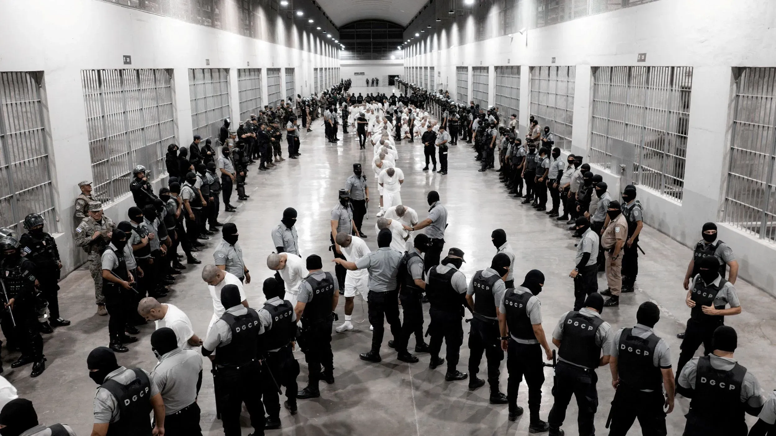 صورة تظهر مجموعة من رجال الشرطة والجنود في سجن، حيث يتجمع المعتقلون في صفوف، مما يعكس الوضع الأمني المشدد في السلفادور.