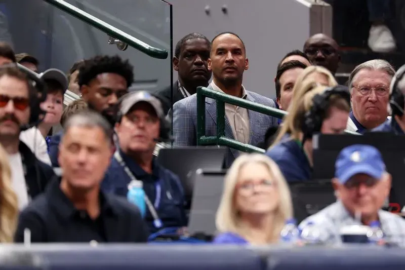 مشجعو دالاس مافريكس في مباراة، يظهرون مشاعر مختلطة بعد تداول لوكا دونشيتش، مع التركيز على المدير العام نيكو هاريسون في الخلفية.