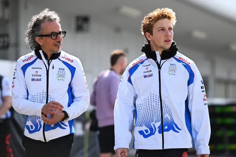 مدير فريق ريد بُل ومساعده يسيران في حلبة سباق، يرتديان ملابس فريق ريد بُل، وسط أجواء سباقات الفورمولا 1.