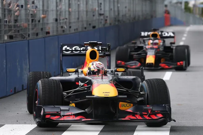 سيارتا ريد بُل للفورمولا 1 تتسابقان على حلبة، مع تفاعل الجماهير في الخلفية، تعكس التوترات حول تبديل السائقين.