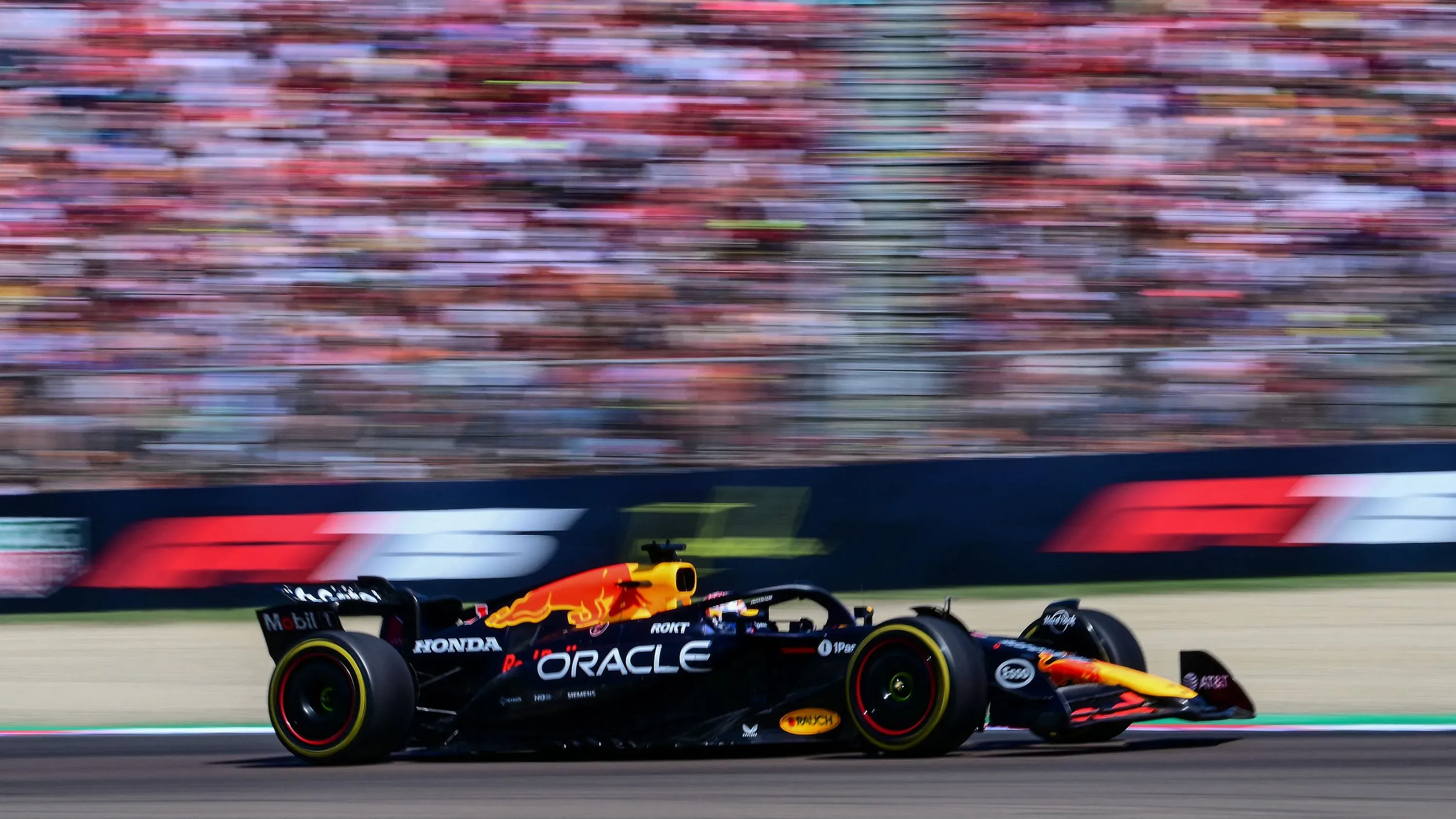 سيارة ماكس فيرستابن من فريق ريد بول تتسابق بسرعة خلال سباق جائزة إميليا-رومانيا الكبرى، مع جمهور متحمس في الخلفية.