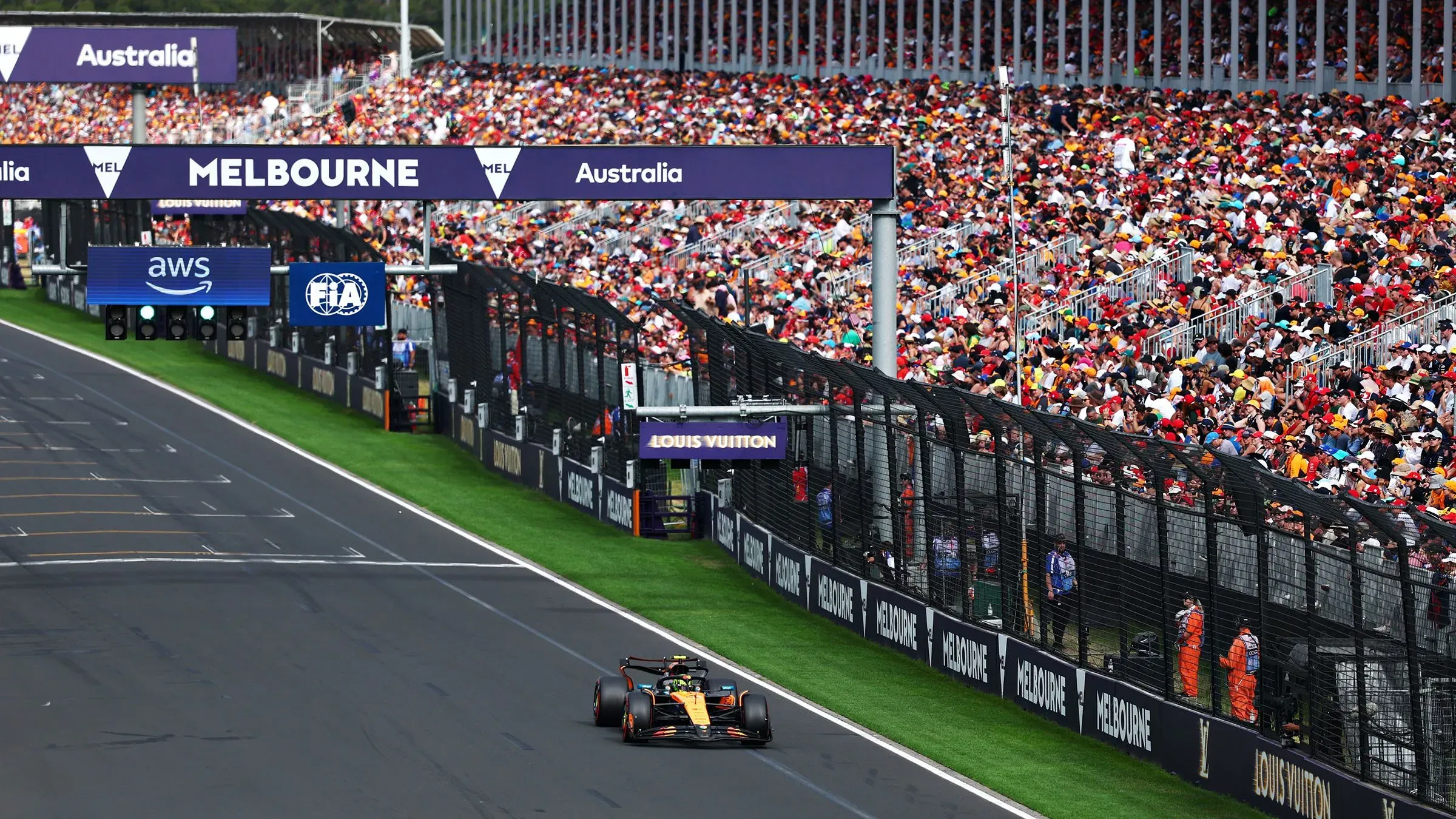 سيارة مكلارين تتسابق في حلبة ملبورن خلال التصفيات الأولى للفورمولا 1 2025، مع جمهور كبير يملأ المدرجات.