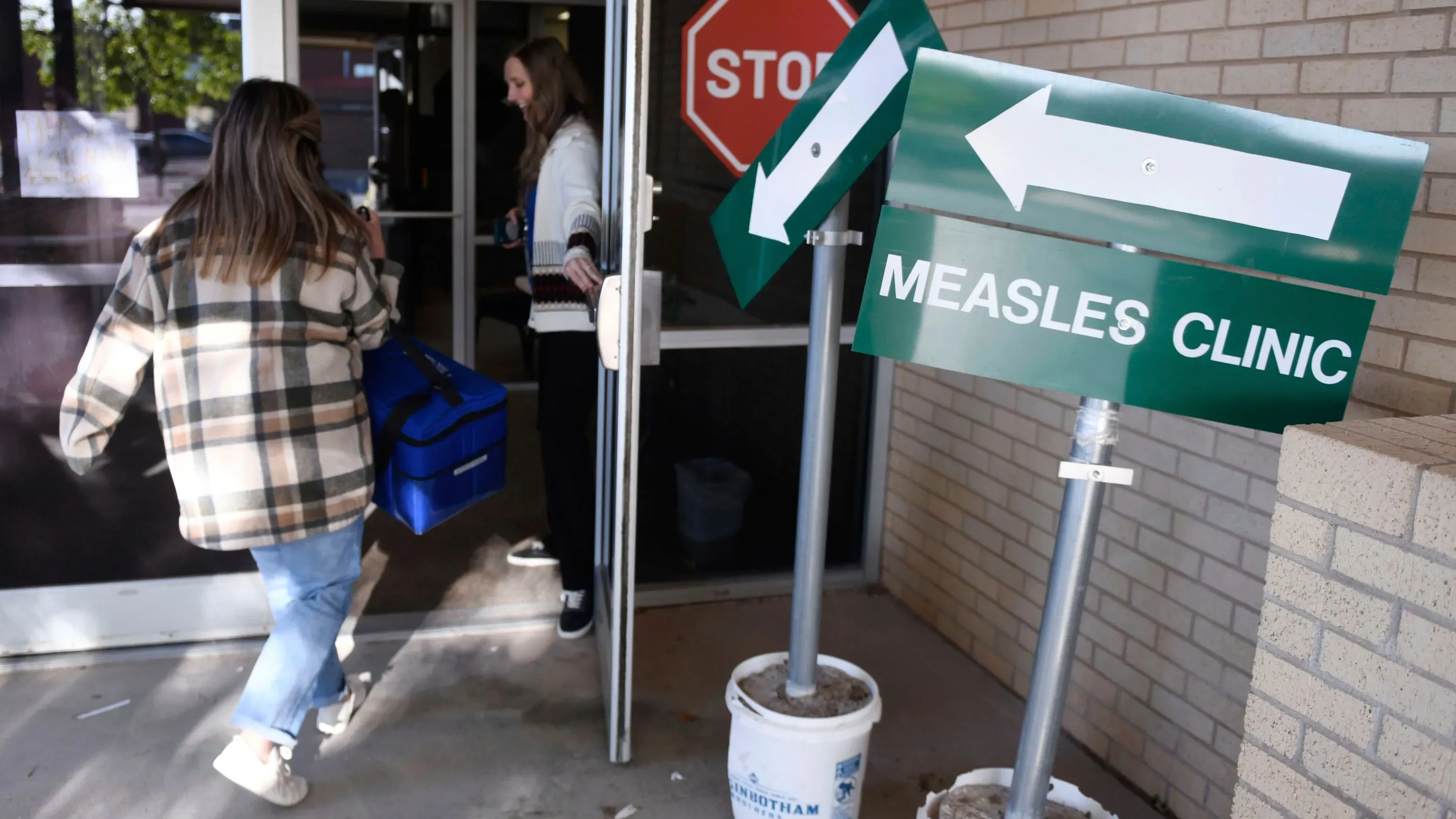 لافتات تشير إلى عيادة الحصبة مع أشخاص يدخلون المبنى، تعكس جهود الاستجابة لتفشي الحصبة في تكساس.