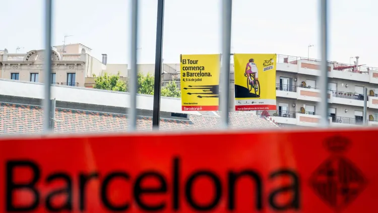 لافتات دعائية للدراجات في برشلونة تظهر خلف حواجز معدنية مع التركيز على شعار المدينة، تعكس أجواء المدينة الرياضية والثقافية.