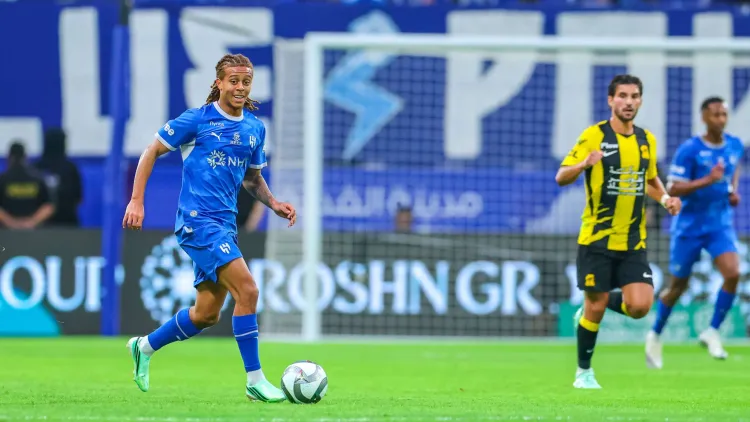 لاعب الهلال بالزي الأزرق يسيطر على الكرة في مباراة دوري روشن السعودي أمام الاتحاد، مع لاعبين من الفريقين في الخلفية.