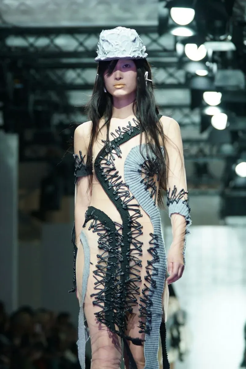 عارضة أزياء ترتدي فستانًا مبتكرًا مصنوعًا من اللاتكس، يظهر تفاصيل معقدة وألوان متداخلة، خلال عرض أزياء في برلين.