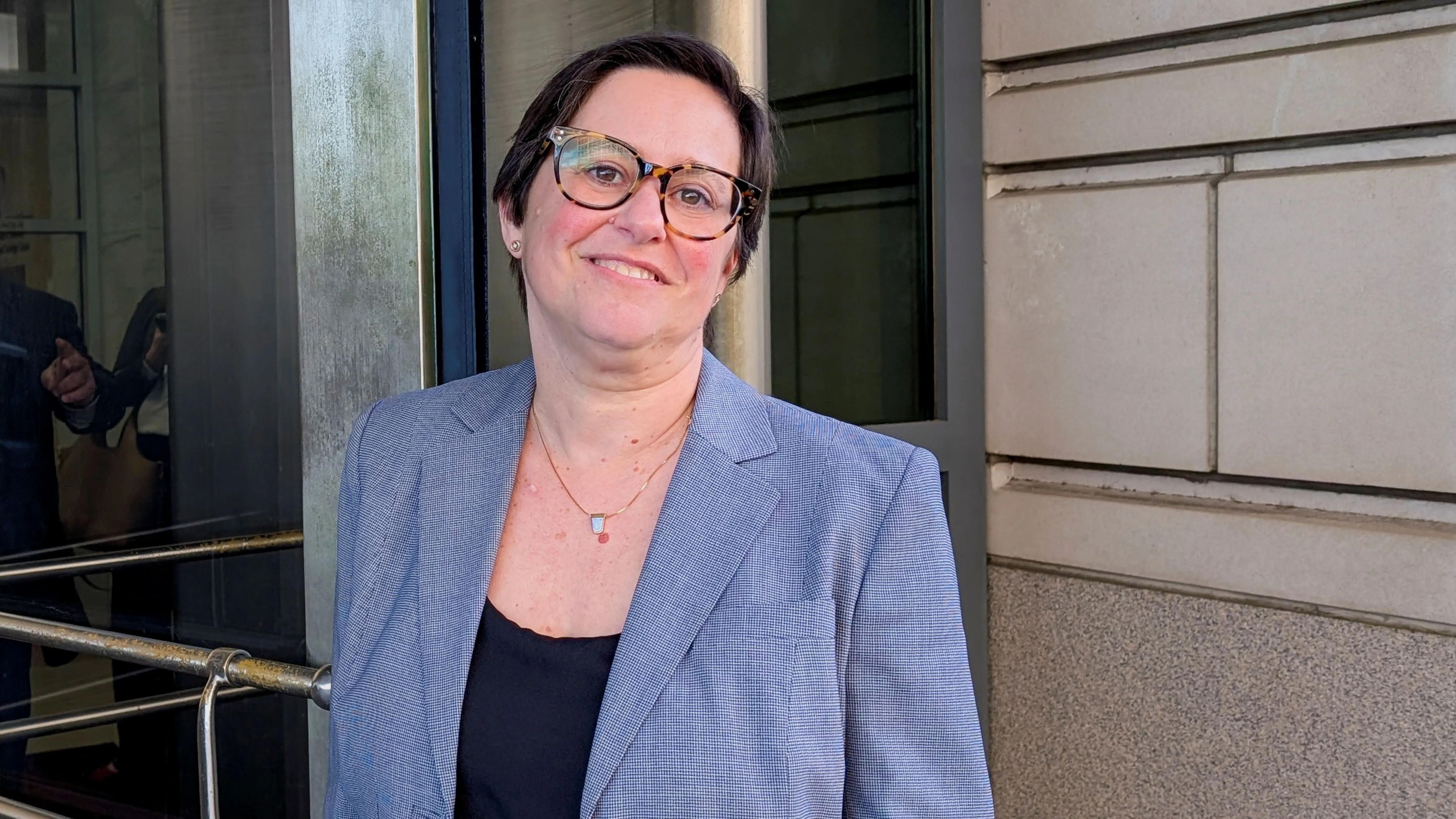 كاثي هاريس، رئيسة مجلس حماية أنظمة الاستحقاق، تقف مبتسمة أمام مدخل المكتب بعد قرار قضائي يسمح لها بالبقاء في منصبها.