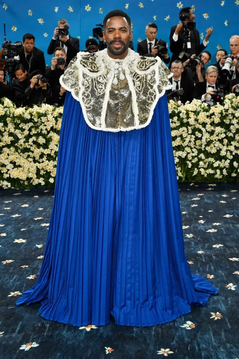 شخص يرتدي زيًا مذهلاً باللون الأزرق مع تفاصيل فضية في حفل الميت غالا، محاطًا بكاميرات وصحفيين في متحف متروبوليتان.