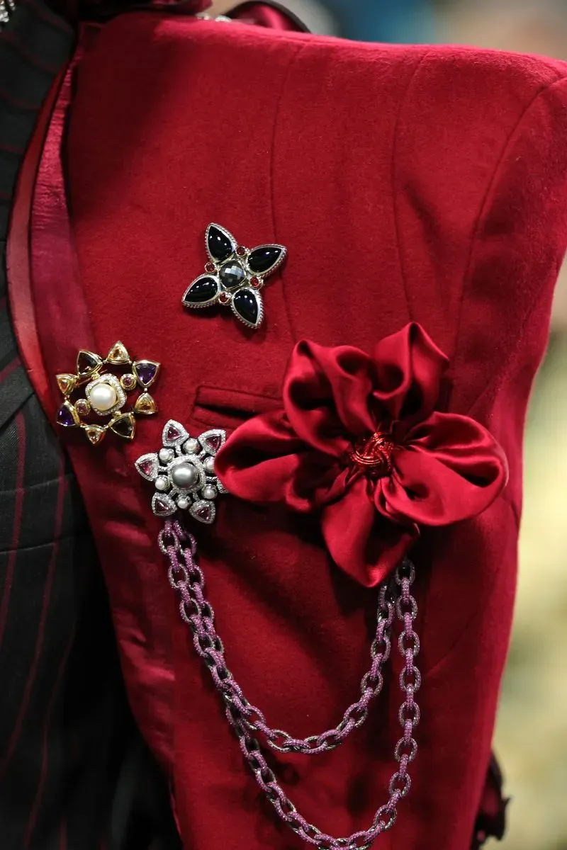 تفاصيل فنية لإطلالة متألقة في حفل الميت غالا، تتضمن زهوراً وأزراراً ملونة على سترة حمراء، تعكس روح الحدث وموضوع الأناقة السوداء.