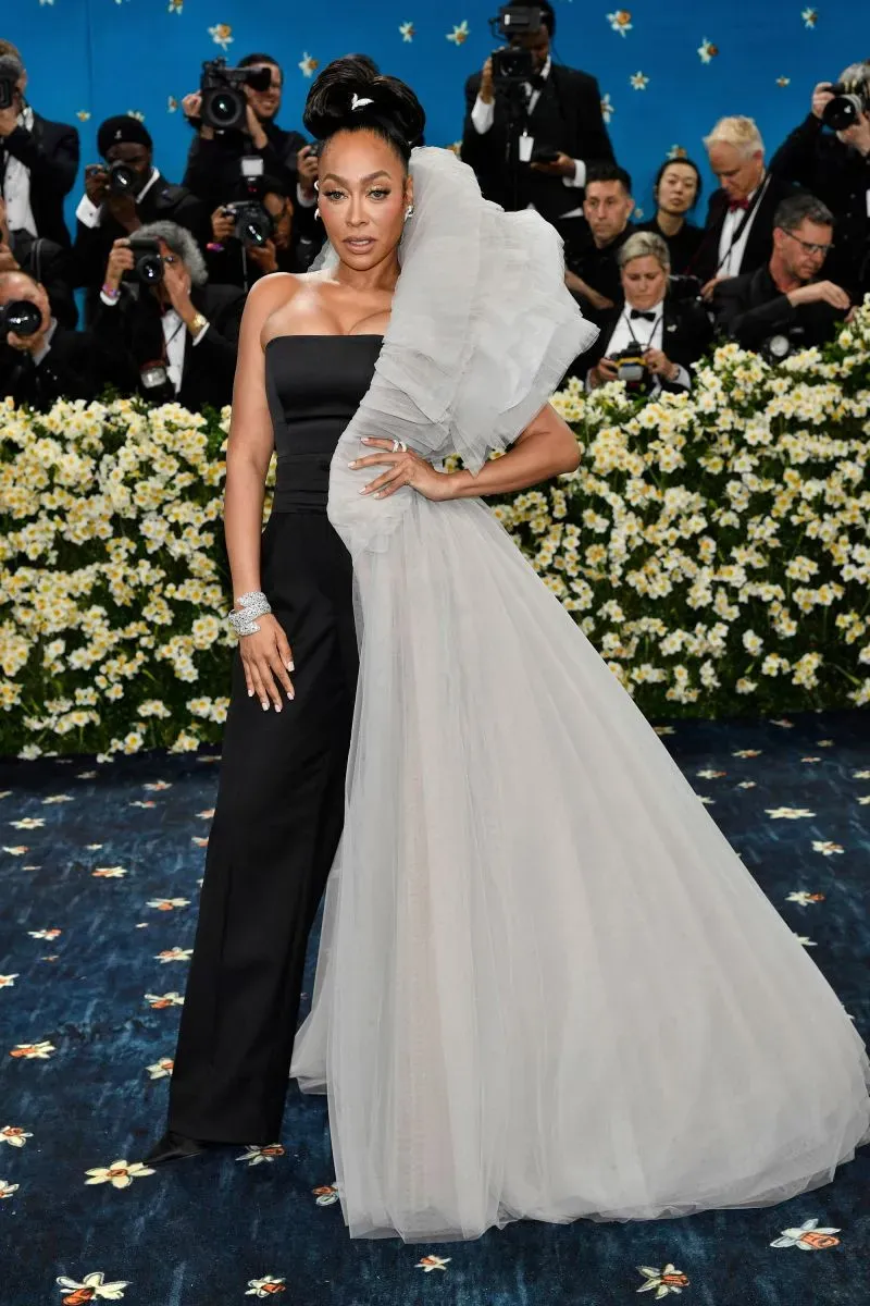 نجمة ترتدي فستاناً أنيقاً يجمع بين الأسود والرمادي مع تفاصيل درامية، تتوسط حفل الميت غالا في متحف متروبوليتان، محاطة بالصحفيين.