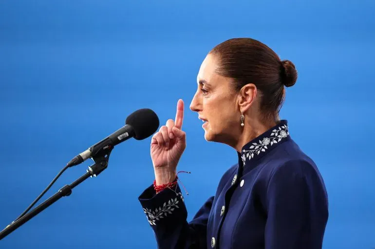 وزيرة الأمن المكسيكية عمر غارسيا هارفوش تتحدث في مؤتمر صحفي، مشيرةً بإصبعها، في خلفية زرقاء، في سياق اعتقال مطلوبين دوليين.