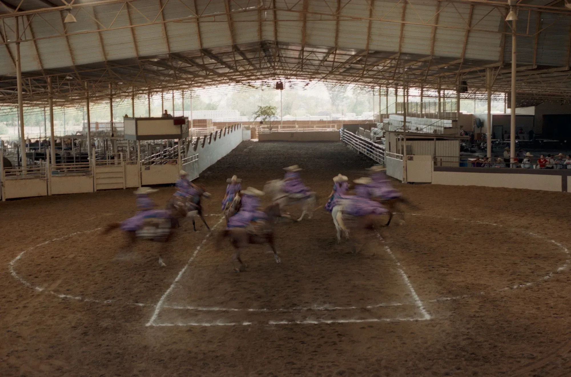 نساء يرتدين فساتين ملونة تتمايل أثناء أدائهن روتين الإسكاراموزا على خيولهن في ساحة مغلقة، مع التركيز على التنسيق والجمال.