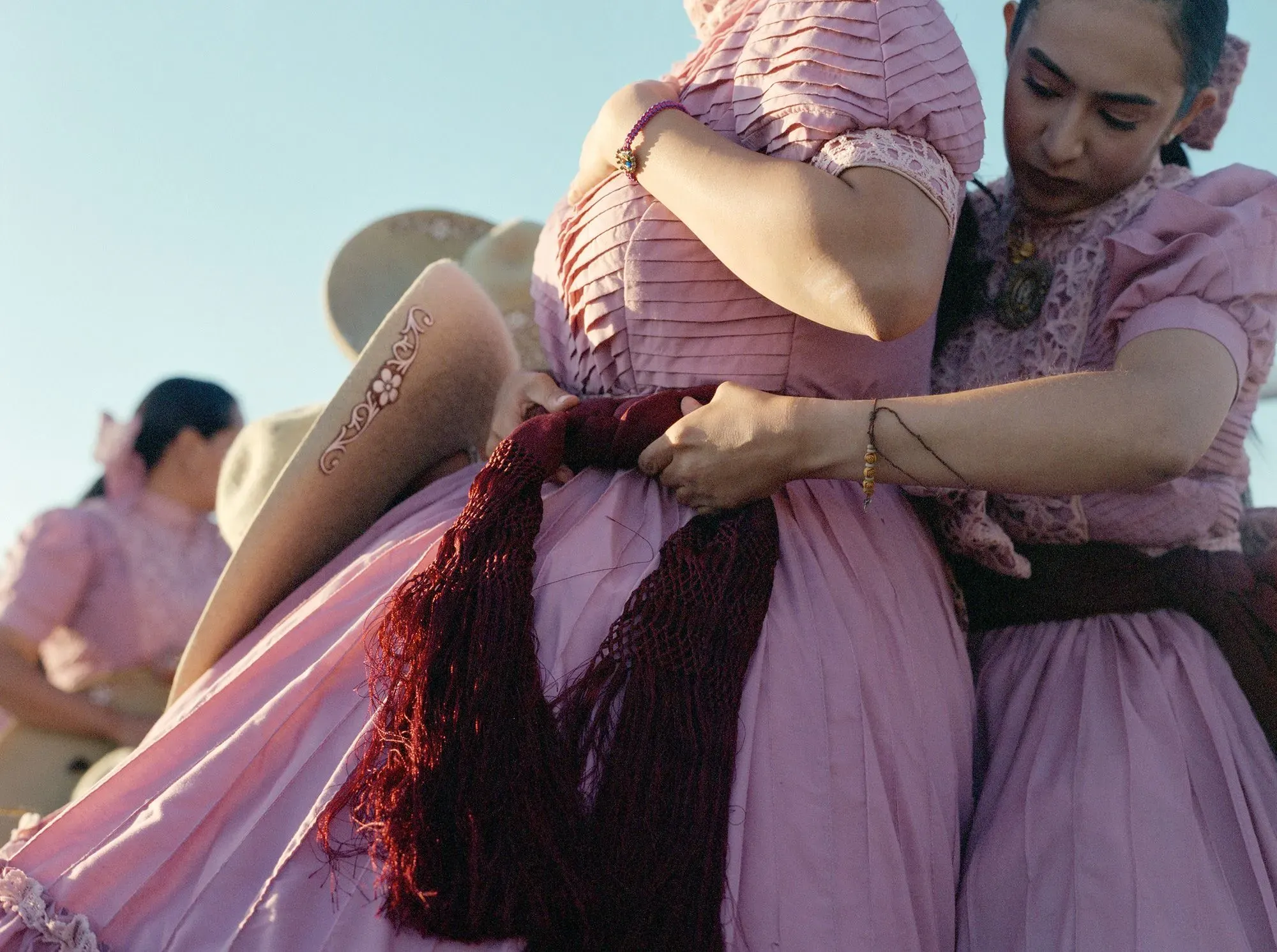 نساء يرتدين فساتين إسكاراموزا الوردية، يتعاونن في ربط الأشرطة قبل المسابقة، مع التركيز على تفاصيل الزي التقليدي.