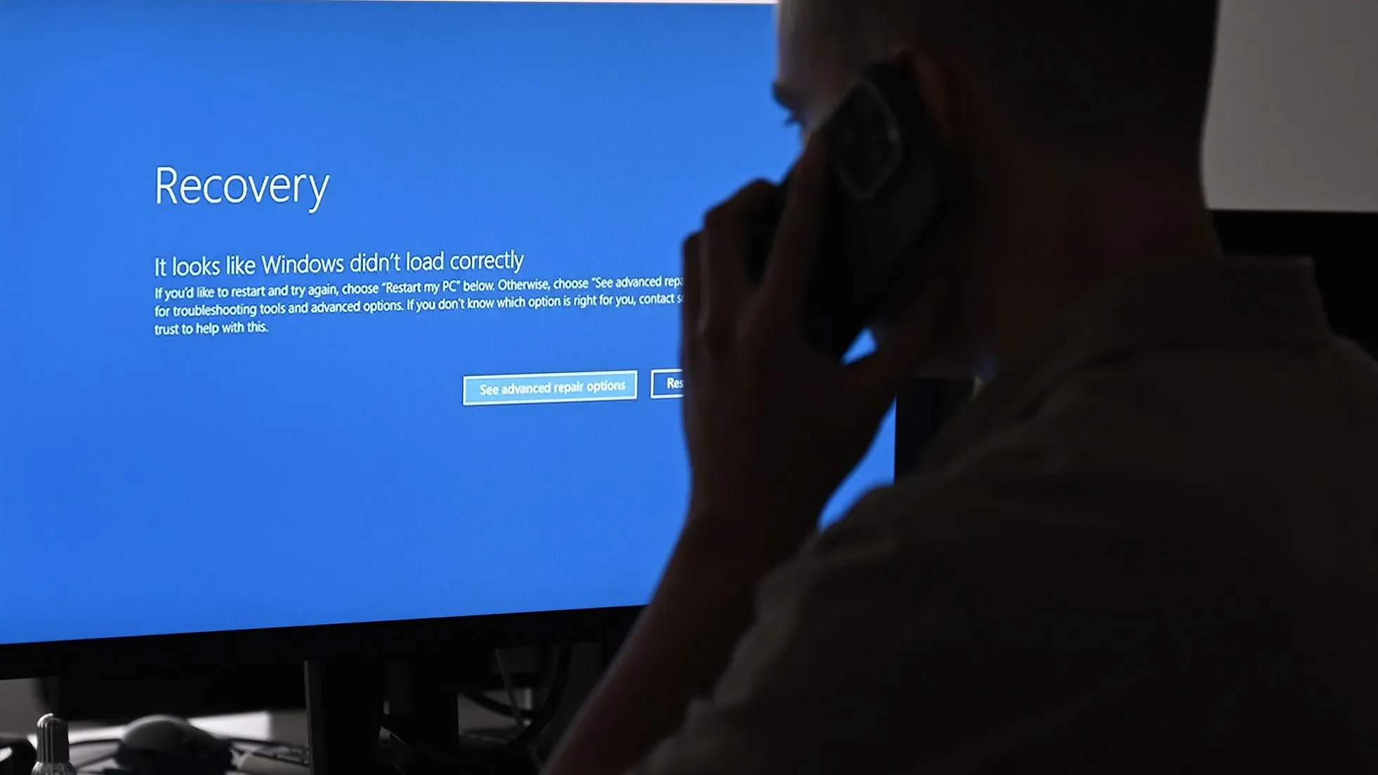 شاشة زرقاء تعرض رسالة "استعادة" تفيد بأن نظام ويندوز لم يتم تحميله بشكل صحيح، مع شخص يتحدث في الهاتف.