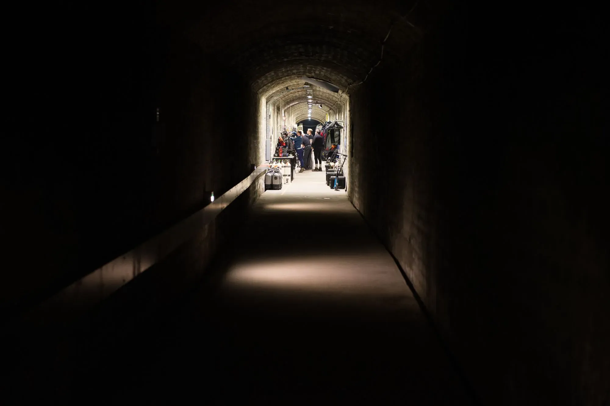 مدخل كهف مولنار يانوس في بودابست، حيث يتجمع الغواصون مع معداتهم في ممر مضاء، محاط بجدران صخرية.