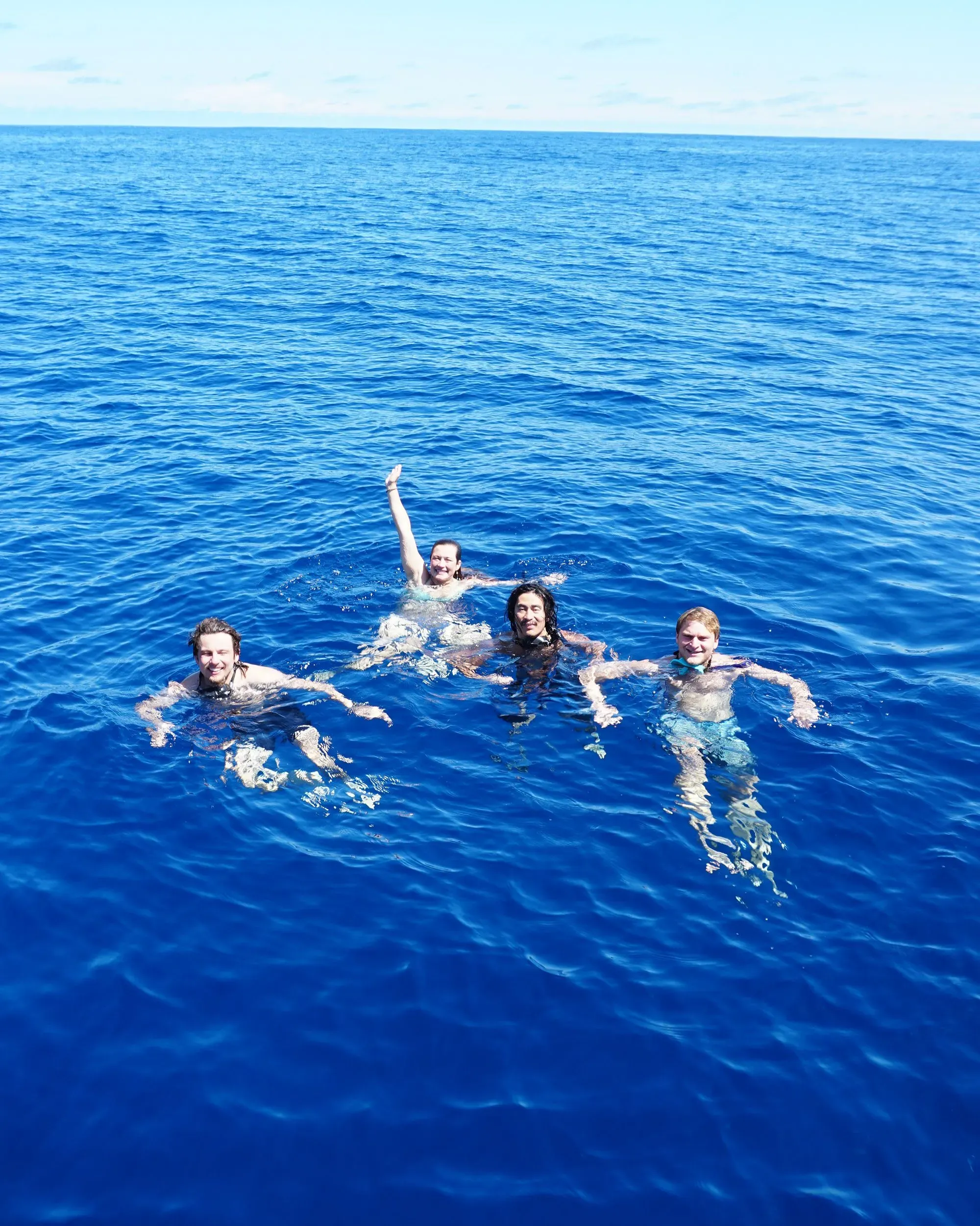 أربعة أصدقاء يسبحون في مياه المحيط الهادئ الزرقاء الصافية، مستمتعين بتجربة الإبحار والمغامرة.